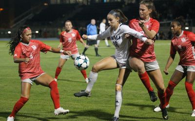 An N A U Soccer match where the N A U athlete has control over the ball but is surrounded on all sides by her opponents.