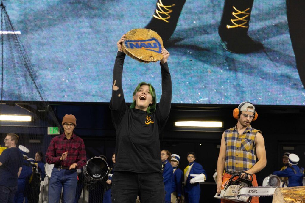 A proud, freshman Lumberjack holds up a tree cookie while cheering to the crowd.
