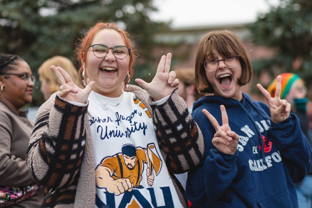 N A U students throw up the Lumberjack hand sign while smiling and enjoying themselves at the homecoming carnival.