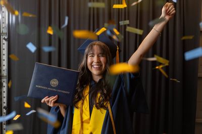 An N A U graduate smiles with excitement while holding their degree.