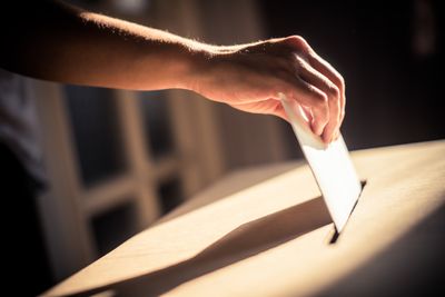 Hand placing a ballot inside a box
