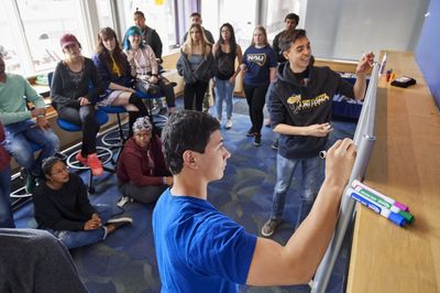 Group of students gathered around a whiteboard writing on it or watching.